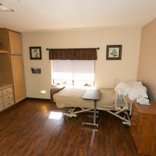 A well-lit hospital room with a single bed, wooden flooring, and minimalistic decor.