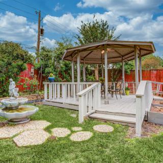 A serene garden setting featuring a white gazebo with surrounding lush greenery and a decorative fountain.