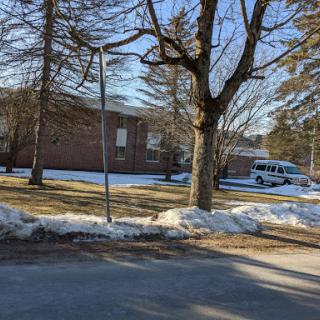 A serene winter scene featuring a building surrounded by snow and bare trees, with a van parked nearby.