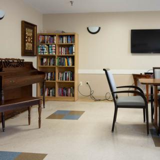 A small library room with a piano, bookshelf, and a seating area.