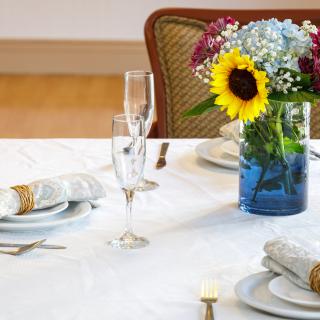 A beautifully arranged dining table with elegant glassware, plates, and a vase of colorful flowers including a sunflower centerpiece.