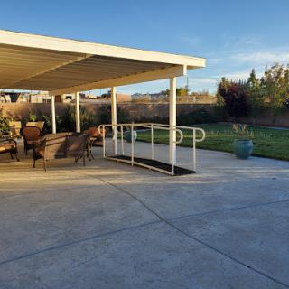 A serene outdoor patio area featuring comfortable seating and an accessible ramp leading to a grassy space, illuminated by the warm glow of sunset.