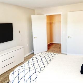 A minimalist bedroom with a TV mounted on the wall, a dresser, and an open closet.
