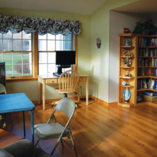 A cozy living room with a desk by the window and a bookshelf.