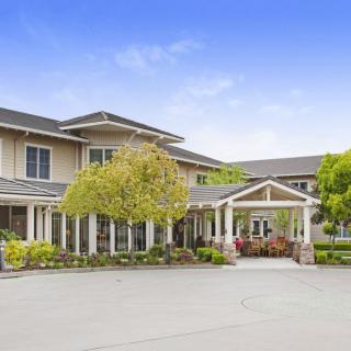 A two-story residential building with a landscaped driveway and trees.