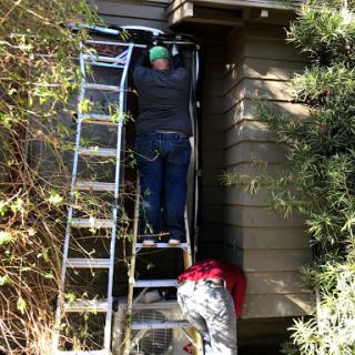 Workers using a ladder to perform maintenance on a house.