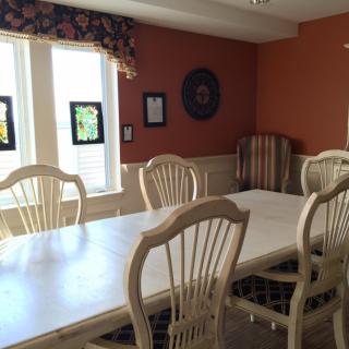 A sunlit dining room with a large table and chairs, featuring warm-colored walls and wall decor.