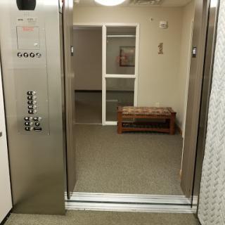 A view of an elevator entrance leading to a hallway with a bench.