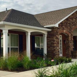 A suburban house with a brick exterior, featuring a front porch and well-maintained landscaping.