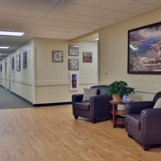 A quiet hallway with a seating area featuring two chairs, a small table, and a painting on the wall.