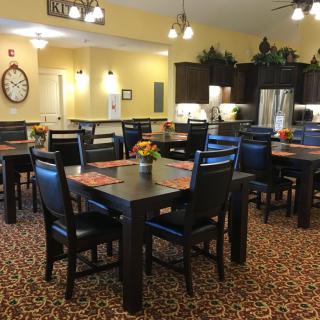 A cozy dining area with multiple tables and chairs, featuring a kitchen in the background.