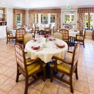 A neatly arranged dining room with round tables and upholstered chairs.