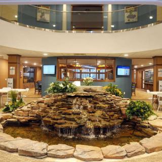 A modern lobby featuring a central fountain with cascading water surrounded by seating and architectural details.