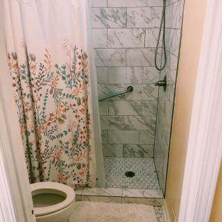 A compact bathroom featuring a tiled shower and a toilet with a floral curtain.