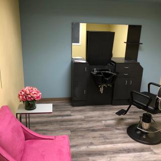 A modern hair salon interior featuring a styling chair, mirror, and pink sofa with decorative flowers.