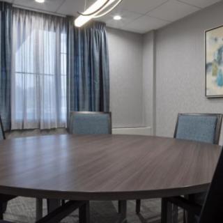 A modern conference room with a round table and chairs, complemented by curtains and wall artwork.