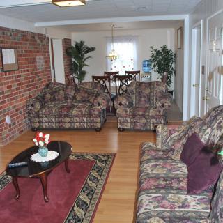 A cozy living room with a brick accent wall, floral-patterned sofa set, and a wooden coffee table on a red carpet leading to an adjoining dining area.