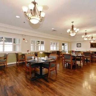 A spacious and elegantly decorated dining area with wooden floors, well-arranged tables and chairs, and decorative chandeliers.