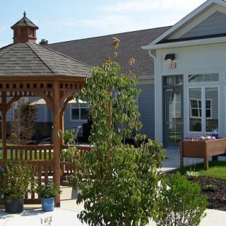 A well-maintained garden with a wooden gazebo and a modern house in the background.