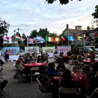 An outdoor community gathering featuring various international flags, as guests enjoy dinner in a festive atmosphere.