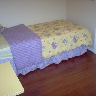 A neatly made bed with floral and striped bedding in a room with wooden floors.