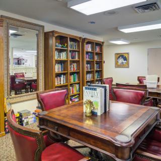 A cozy library reading room with wooden furniture, red chairs, and bookshelves filled with books.