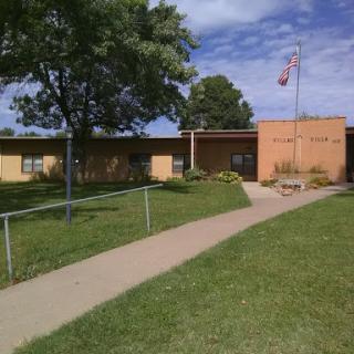 A school building set in a green landscape with a clear pathway leading to the entrance.