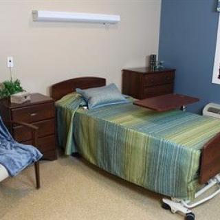 A hospital room featuring a single bed with striped bedding, bedside tables, and a chair.