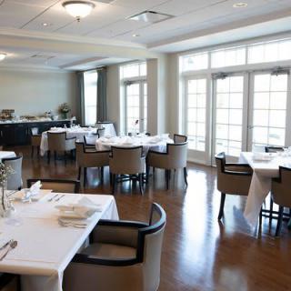 An elegant restaurant dining room with neatly arranged tables and chairs, featuring large windows that allow natural light to fill the space.