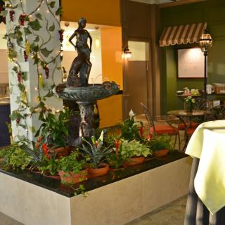 A cozy restaurant interior featuring a decorative statue fountain surrounded by plants.
