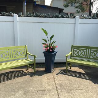 Two green benches flank a potted plant in an outdoor garden setting.