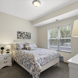 A cozy bedroom with a neatly made bed and natural light coming through a large window.