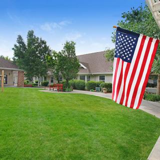 A well-maintained lawn with an American flag and buildings in the background on a clear day.