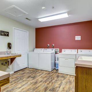 A spacious laundry room equipped with washing machines and a dryer, featuring wooden flooring and a countertop.