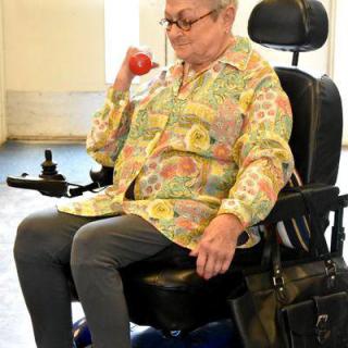 An elderly woman in a wheelchair lifting a dumbbell indoors.