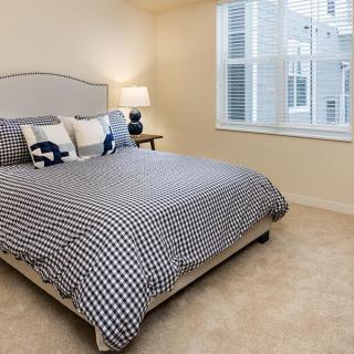A cozy bedroom with a checkered bedspread and decorative pillows, featuring a bedside lamp and a large window.