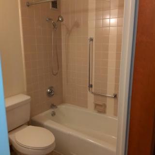 A compact bathroom featuring a bathtub with a shower, toilet, and tiled walls.