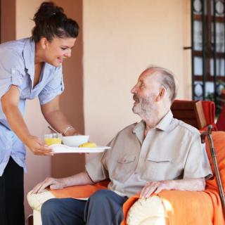 A caregiver provides a meal to an elderly man.