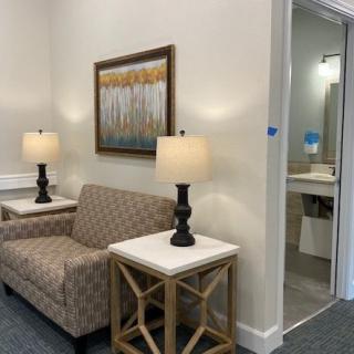 A cozy waiting room with a patterned sofa, two lamps on side tables, and a framed artwork on the wall.
