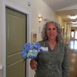A woman standing in a hallway holding a bouquet of blue flowers.