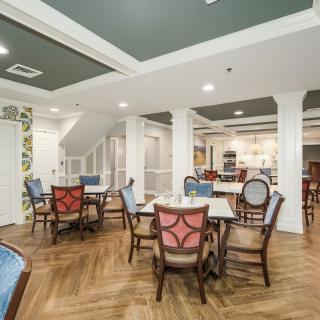 A well-lit dining area with wooden flooring, featuring multiple tables and chairs arranged for guests.