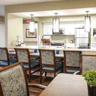 A modern kitchen and dining area featuring a large counter with several chairs, illuminated by stylish pendant lights.
