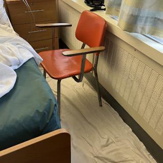 A view of a hospital patient room featuring an orange chair beside a bed.