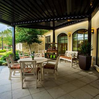 A cozy outdoor patio with seating under a pergola, surrounded by greenery.