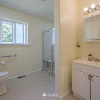 A clean, minimalist bathroom featuring a toilet, shower, and vanity with mirror.
