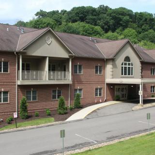 A residential building surrounded by greenery with a driveway leading to the entrance.