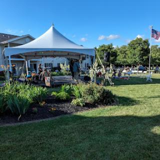 A tent set up for an outdoor event surrounded by lush greenery and a clear blue sky.