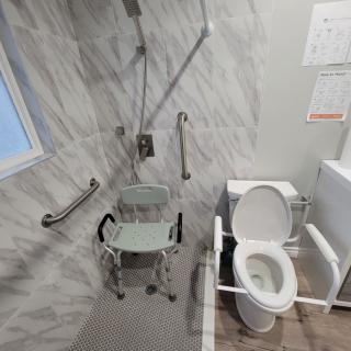 An accessible bathroom with a shower chair and toilet equipped with grab bars.