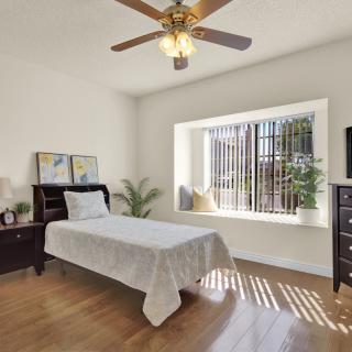 A cozy minimalist bedroom with a single bed, wooden flooring, and ample natural light from a large window.