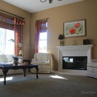 A cozy living room featuring a fireplace, armchairs, and a coffee table, with natural light streaming through the windows.